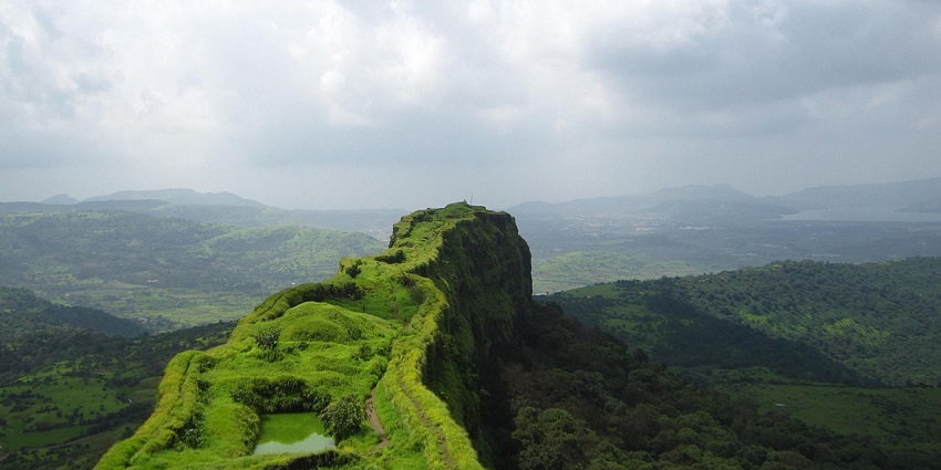 A view from the top of Lohagad Fort shows a long stretch of green hills under a bright sky.