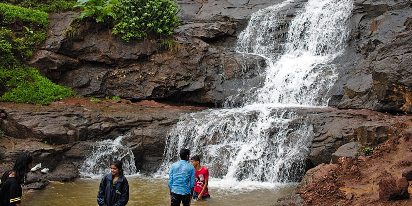 Waterfall in Lonavala cascading down through mountains with people enjoying still water.