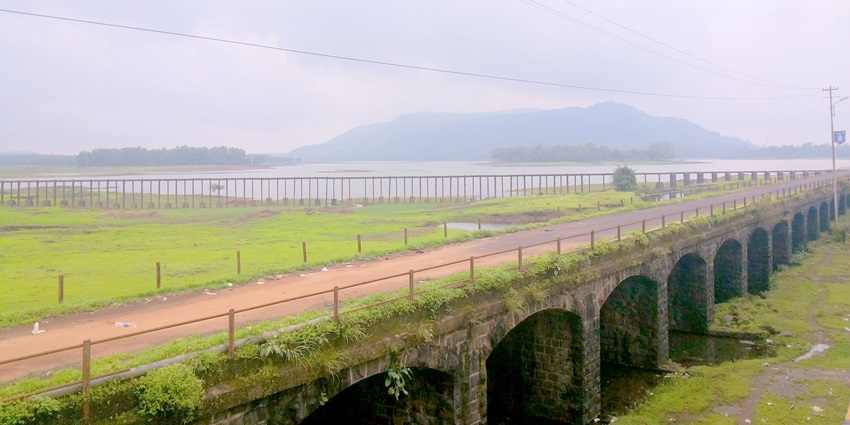Wide view of Lonavala Lake surrounded by greenery, calm waters, and a cloudy sky in India.
