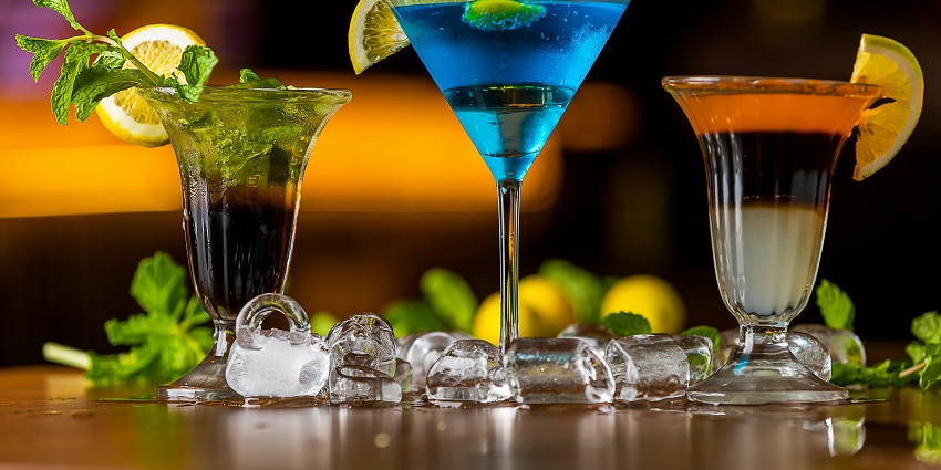 A photo of cocktail drinks in 3 different colours with lime and mint garnishing.