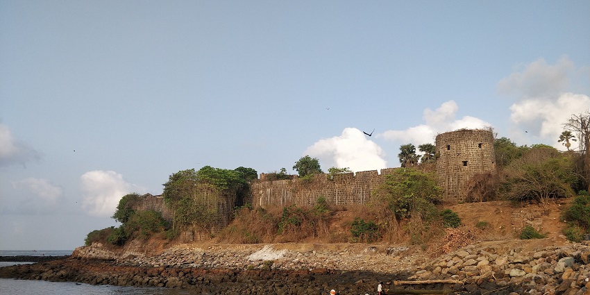 stone walls and bastions of madh Fort standing along a rocky coastline under a clear sky