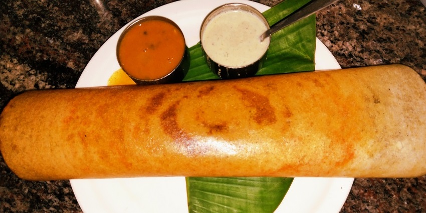 Golden dosa served with coconut chutney and sambar served on a plate with banana leaf