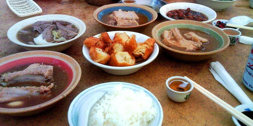 Chinese Food Dishes on a table in different bowls and a man holding one of them.