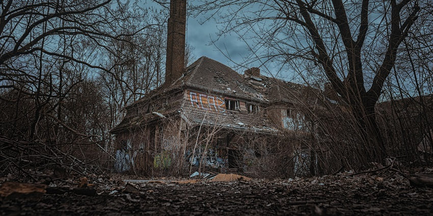A picture of an abandoned house taken from the outside with spooky surroundings