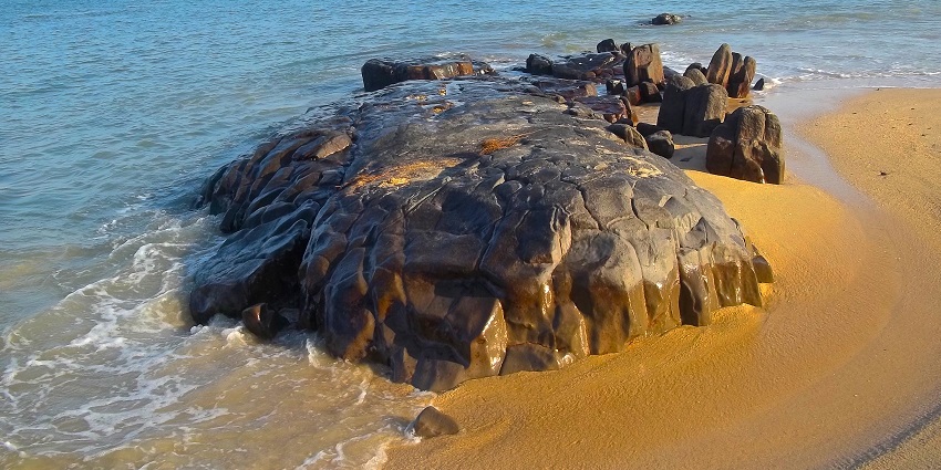 Water splashes over sand and a large rock at Malpe Beach, a tourist attraction in Udupi.