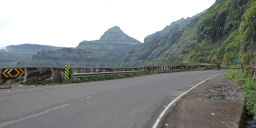 A picture of a road moving through the scenic western ghats with a rugged hill in the background