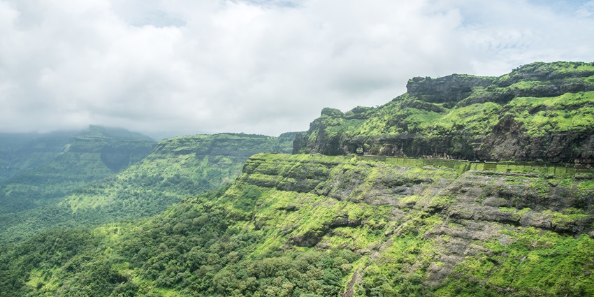 Scenic view of Malshej Ghat with winding mountain road, lush greenery, and misty hills