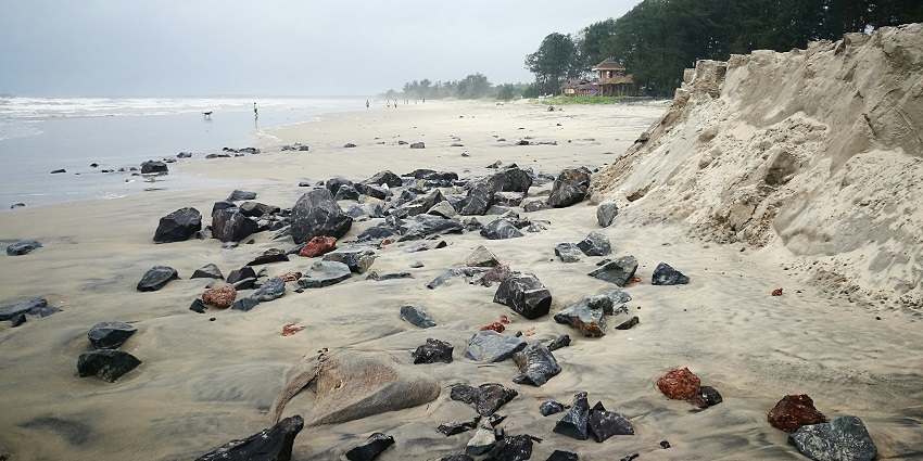 A glimpse of the pristine white shoreline of a beach in Malvan decked with giant rocks.