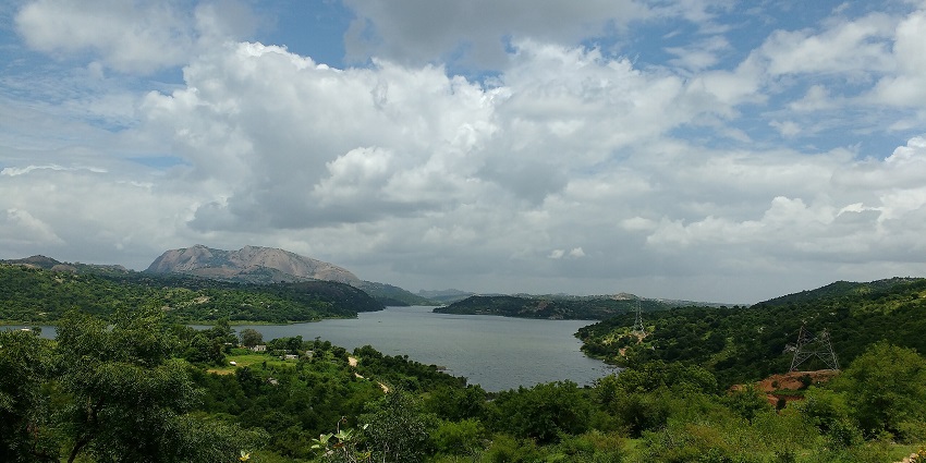 A wide, lush valley with a lake nestled between rolling hills under a cloudy sky.