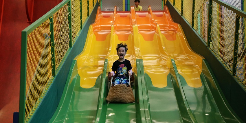An image shows a young boy joyfully sliding down a blue slide through water for adventure.