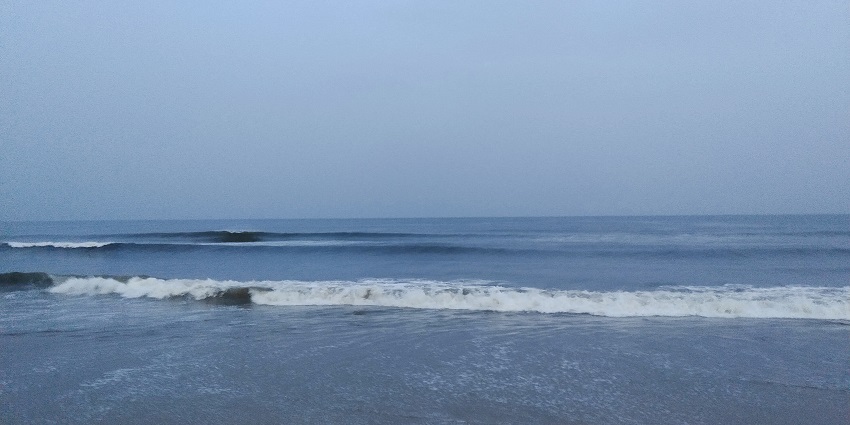Water waves gently hitting the sandy shore of Marina Beach under the clear blue sky.