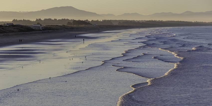 Golden hour at a serene beach with gentle waves, scattered people, and distant mountains