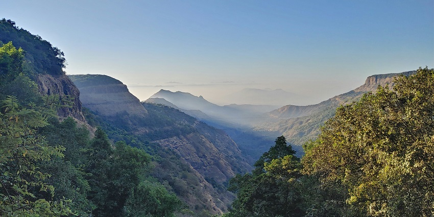 Serene waterfall cascading down rocky cliffs, surrounded by lush greenery during the day.