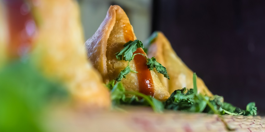 Three samosas are placed on a brown tray garnished with ketchup and coriander leaves.
