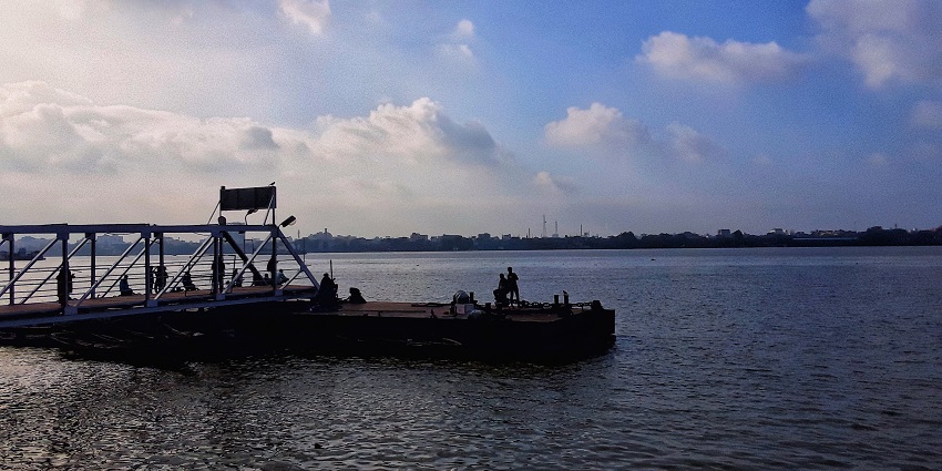 Scenic riverside view with a jetty extending into calm waters under a clear afternoon sky.
