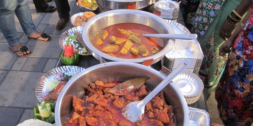 Variety of Koli fish displayed in steel containers and aluminium foils with a lady standing.