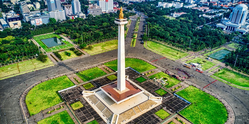 An image of the Monas Tower building with modern architectural design, standing tall against a clear blue sky.