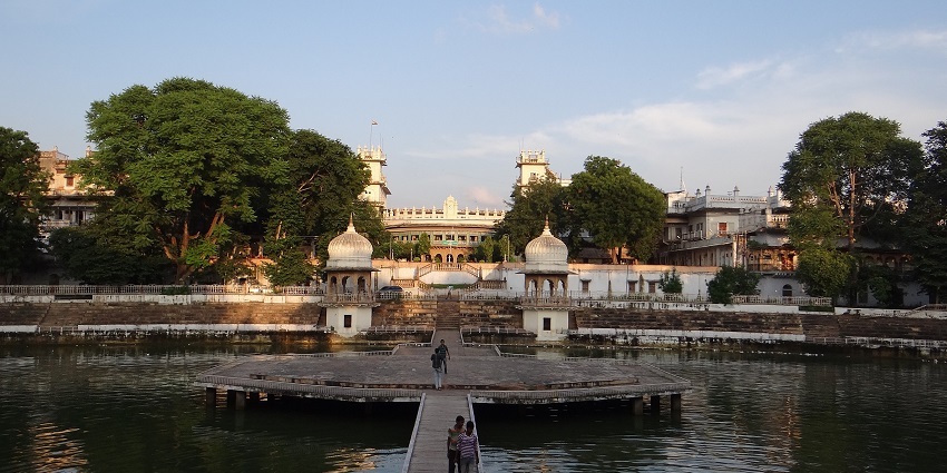 A distant view of Moti Mahal surrounded by water and people taking pictures in front of it.