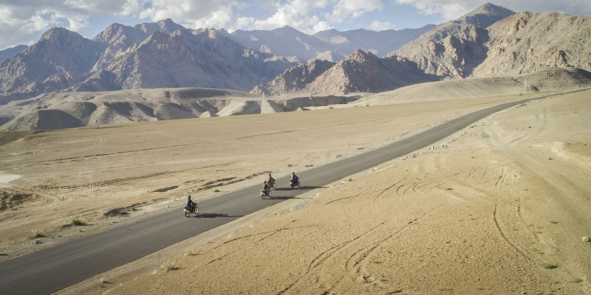 An aerial picture of people riding motorcycles on a road in Ladakh with scenic mountains in the background
