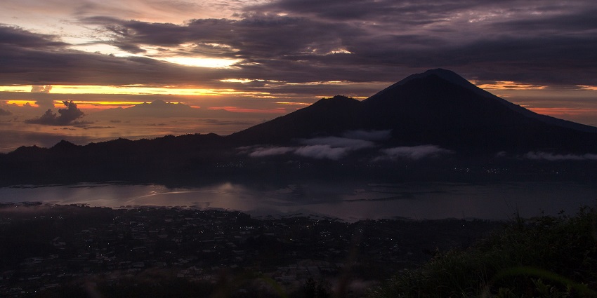 Panoramic view of sunrise at Mount Batur with surrounding lake, morning sky and clouds.