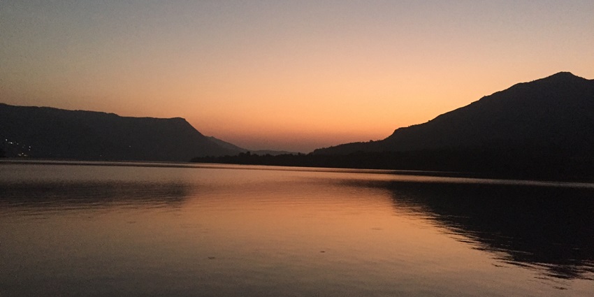 The tranquil waters of Mulshi Lake reflect green hills and scattered clouds around the dam.