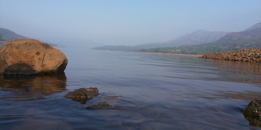 Mulshi Lake with calm water, rocks and surrounding hills covered in mist for kayaking in Lonavala.