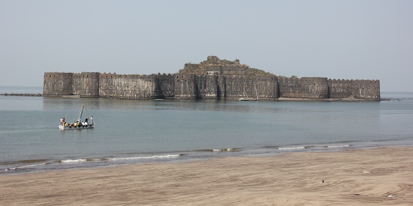 A wide view of the Murud-Janjira Fort, a boat loaded with people in the foreground