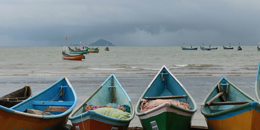 A picture taken at the the shore of Murudeshwar Beach with multiple boats parked and the vast sea in the background