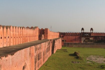 A stone archway leads into Nagardhan Fort, surrounded by trees and lush greenery under a clear sky.