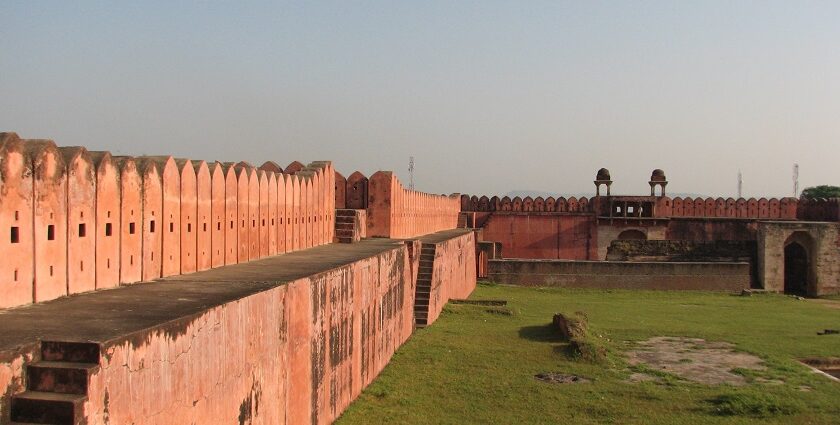 A stone archway leads into Nagardhan Fort, surrounded by trees and lush greenery under a clear sky.