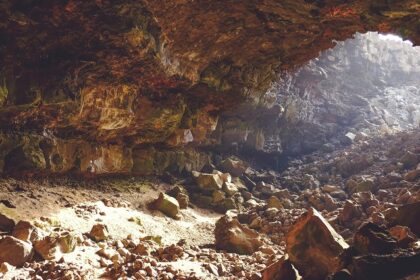 Sunlight peeks through the upper hollow of a cave, with rocks of various sizes inside.