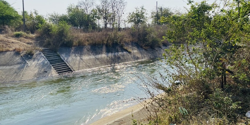 A picture of a tranquil canal flowing around a dam near Wardha, surrounded by greenery