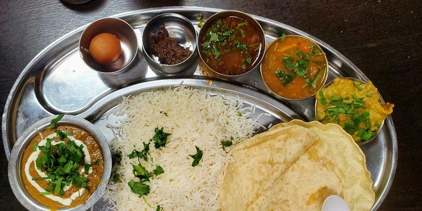 Several Maulpuas are kept on a white round plate, which is placed on a wooden table