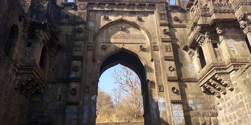 View of the an archway in Narnala fort and the tall trees and clear blue sky