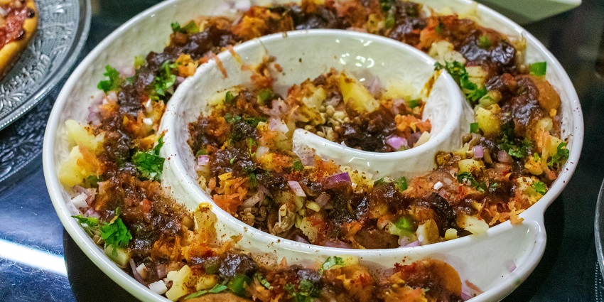 Aloo Chaat, topped with onions, sprouts, sev, papdi, and coriander served in a spiral bowl