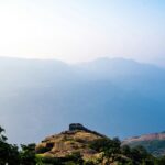 A view of Rajmachi in Maharashtra with lush hills and cloudy skies in the background.