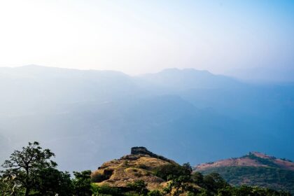 A view of Rajmachi in Maharashtra with lush hills and cloudy skies in the background.