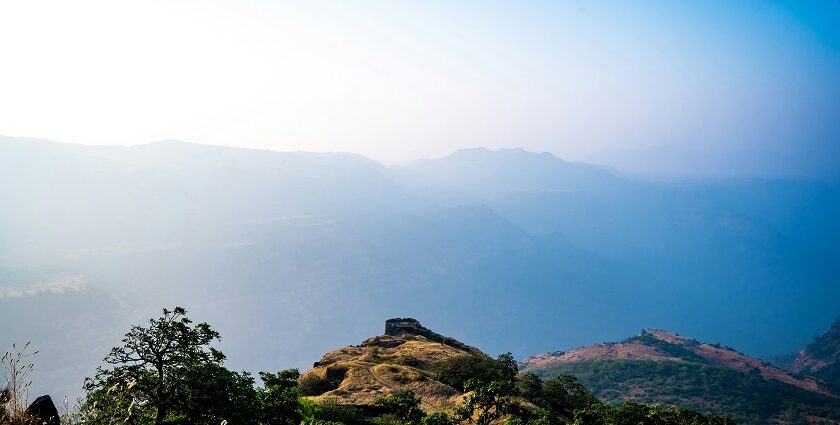 A view of Rajmachi in Maharashtra with lush hills and cloudy skies in the background.