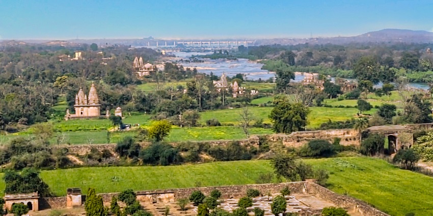 A scenic view of Orchha Fort with the Betwa River flowing beside it in the backdrop.