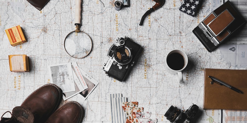 An image of travel things: a camera, a pair of brown shoes, a magnifying lens and more.