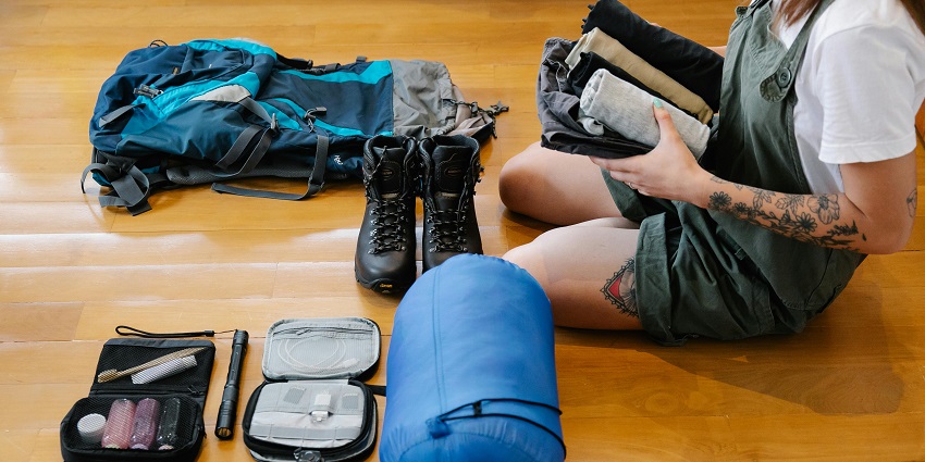 A person packing for a trip with their things like clothes and shoes laid out in front of them.
