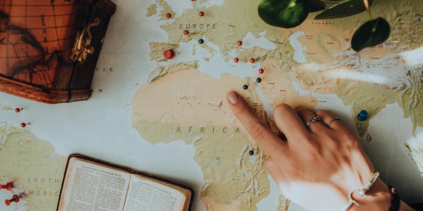 A person pointing at a map with pins on it to mark places and a book over it.