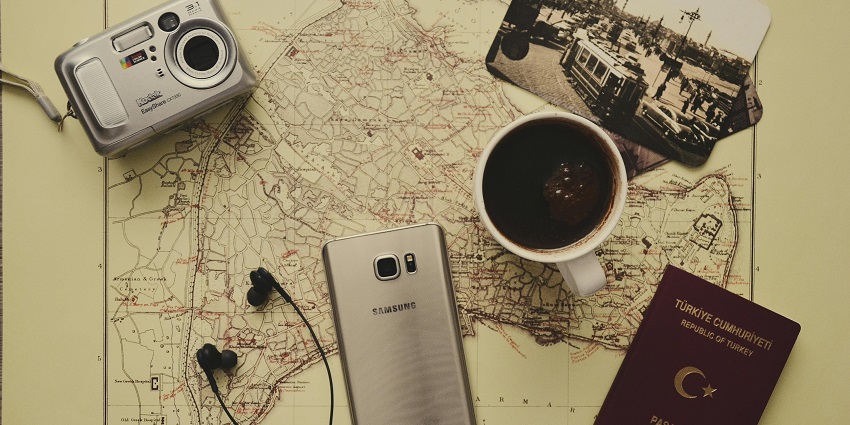A map displayed on a table with a camera, coffee cup, earphones and passport on top.