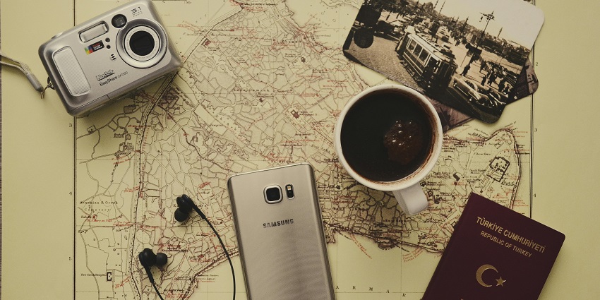 A coffee mug, notebook, earphones, phone and other things displayed over a map on a table.
