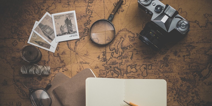 A notebook, pencil, camera and postcards displayed over a map.