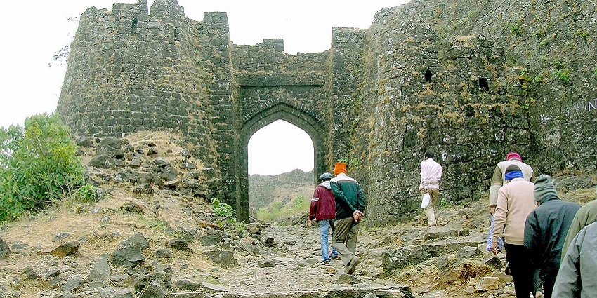 A group of people are walking on an uneven plain and reaching the entrance of Khandar Fort.