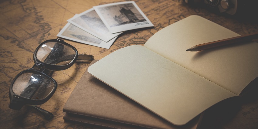 A notebook, spectacles and polaroids displayed over a map on a table.