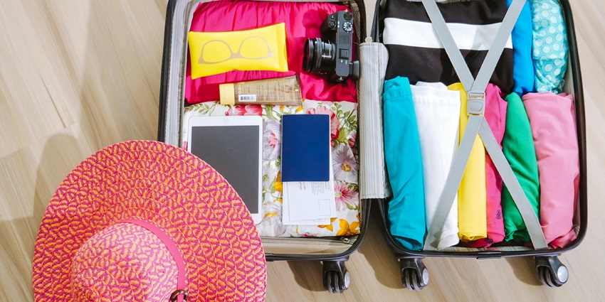 Image of an suitcase with summer clothes, camera packed and a hat on the side