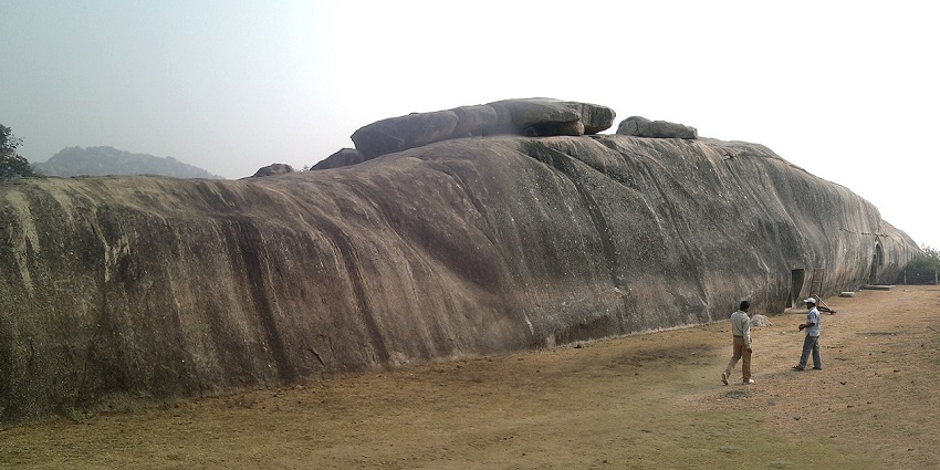 A scenic view of Barabar Caves on Barabar Hills, with rock-cut structures, and people exploring the hills.