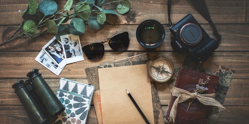 An image of travel things - a camera, a dairy, a binoculars, a compass and more.